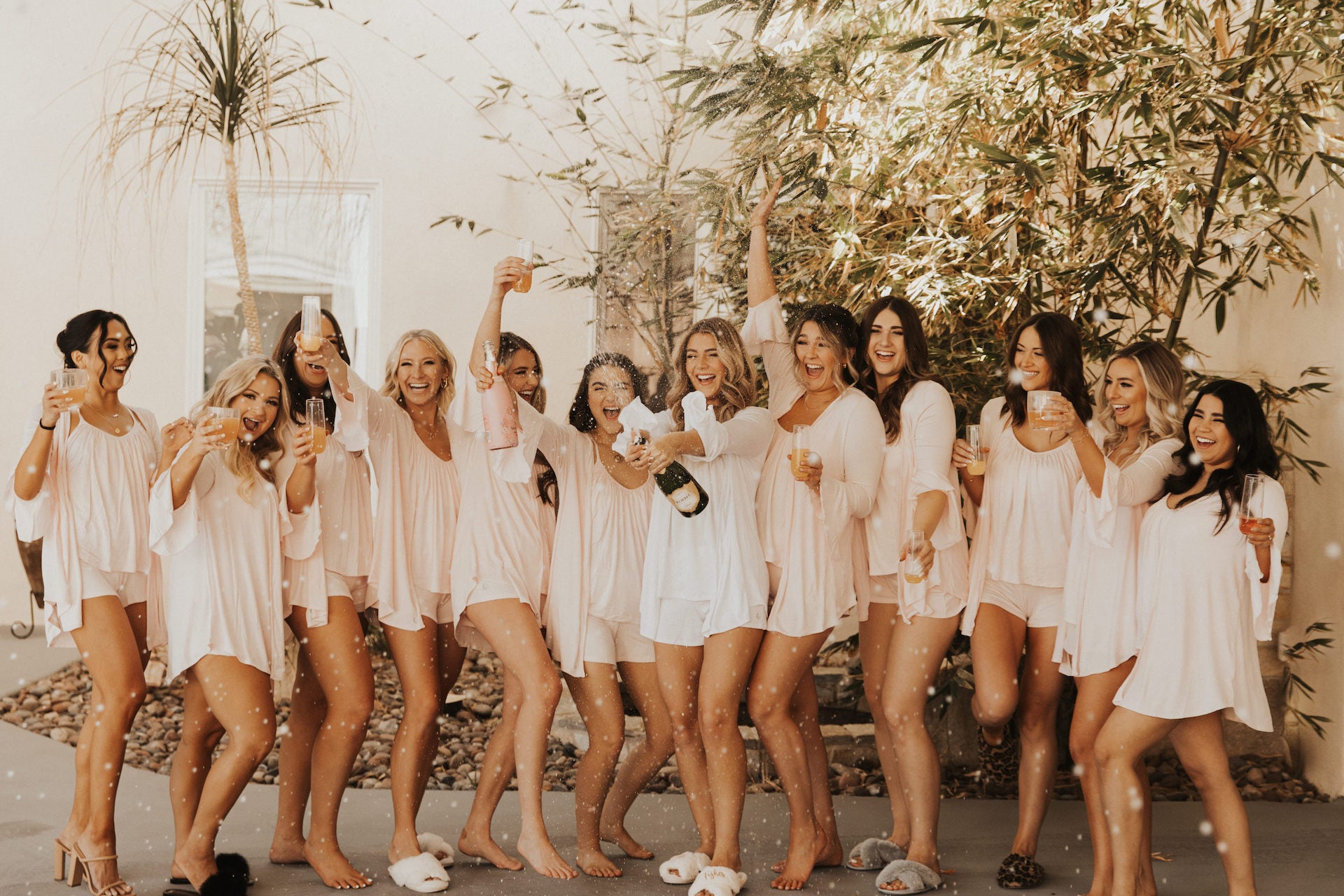 12 bridesmaids lined up wearing JJ Slumber party tops and shorts with the bride popping champagne.